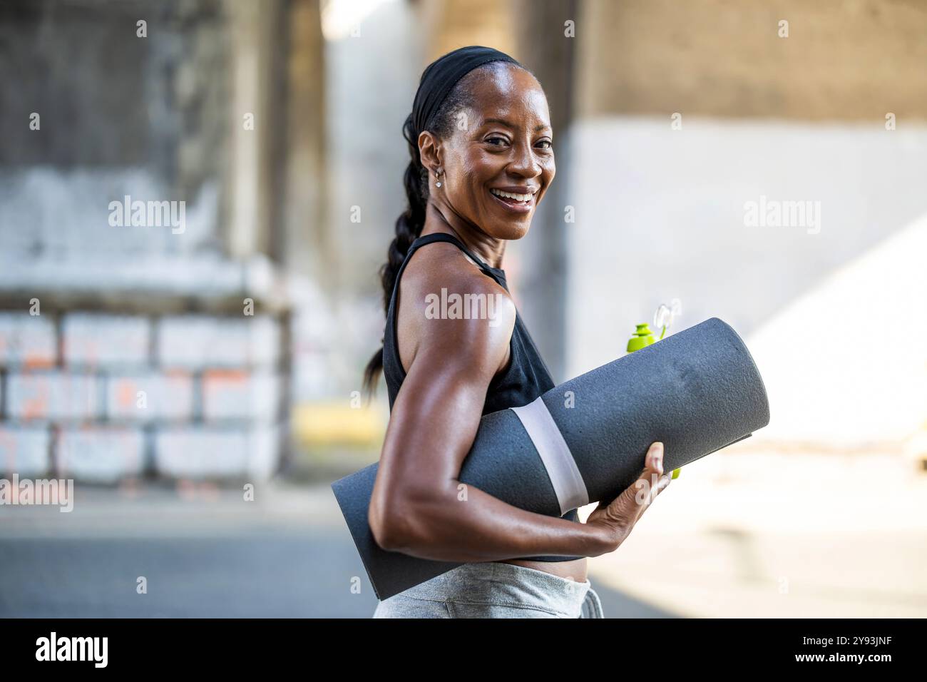 Smiling woman holding an exercise mat in the city street Stock Photo