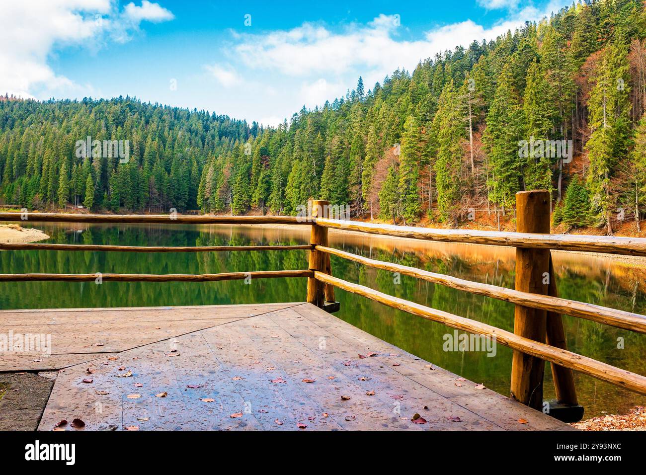 wooden pier on the lake synevyr in autumn. mountain landscape on a sunny day. scenery reflecting in the water. european woodland Stock Photo