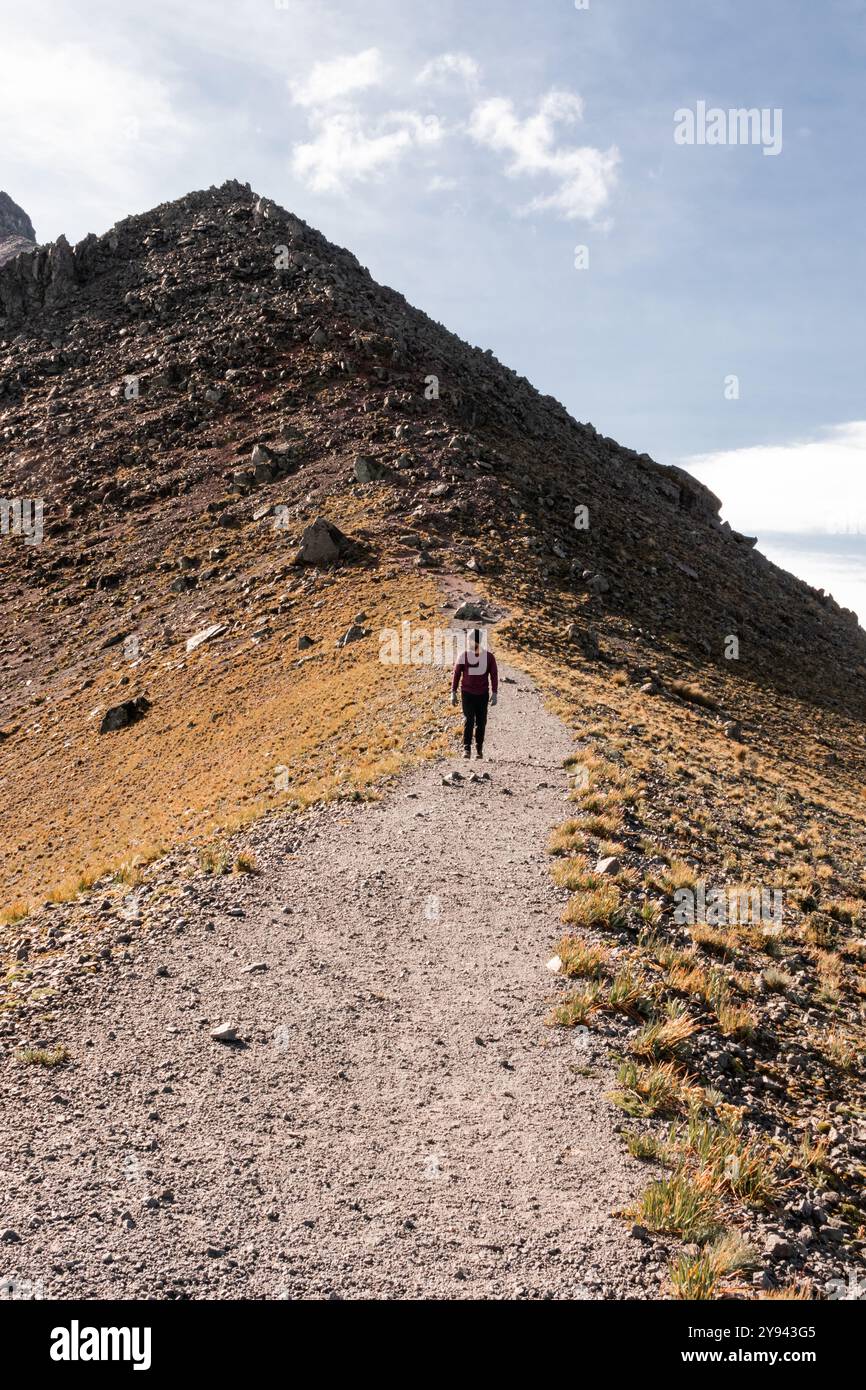 Man walking on a gravel trail amidst rugged mountain terrain under a ...