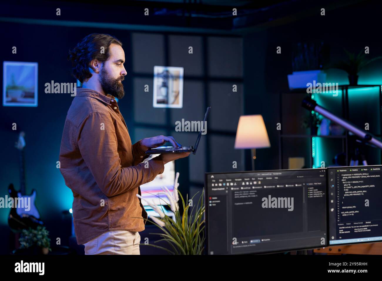 Developer doing software debugging using laptop, checking glitches in lines of code displayed on PC monitors. Man walking around home fixing coding issues using notebook device Stock Photo