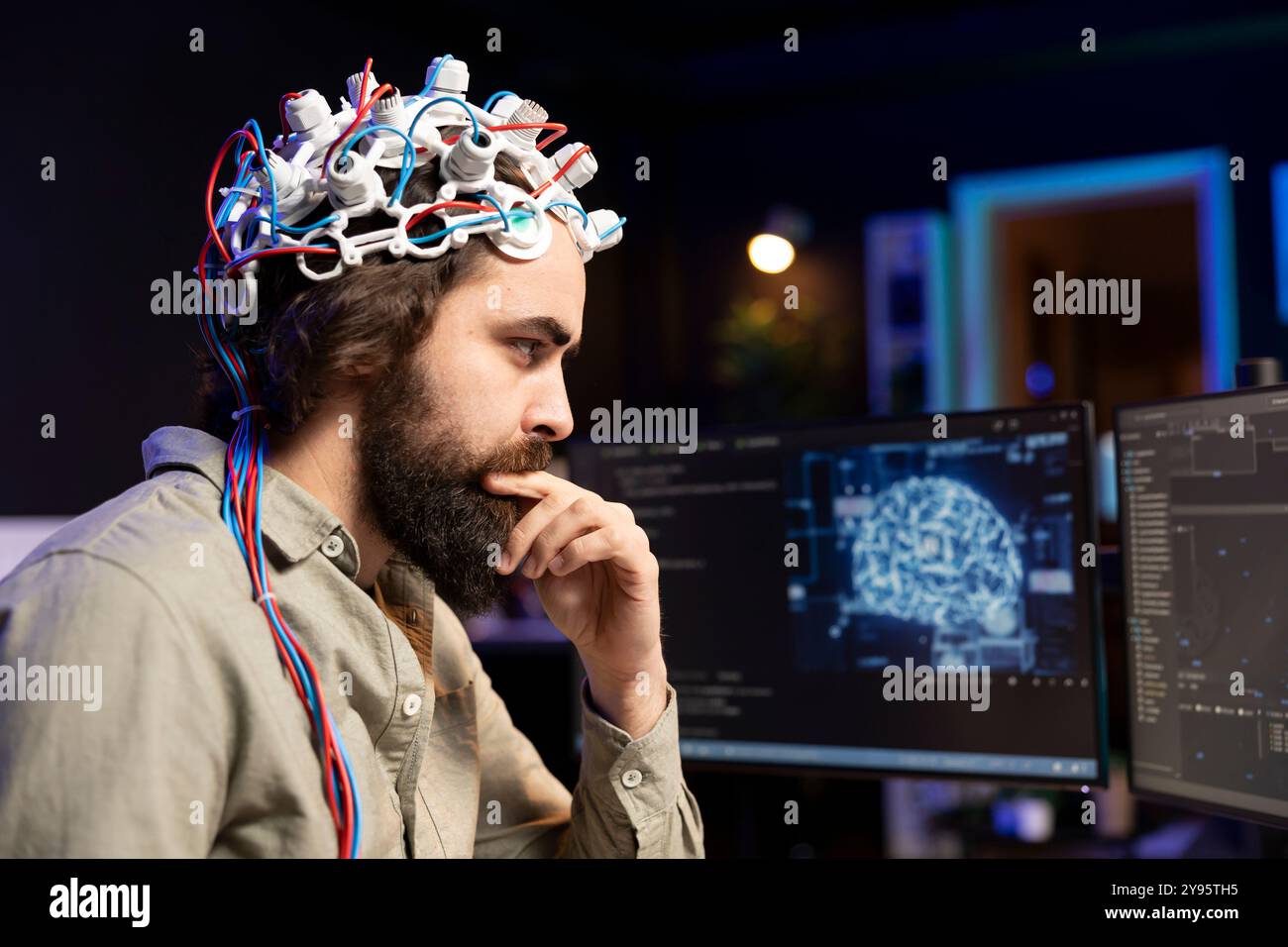 Programmer using EEG headset to upload his mind into computer, attaining immortality. Neuroscientist in apartment experimenting with transferring consciousness into cyberspace Stock Photo