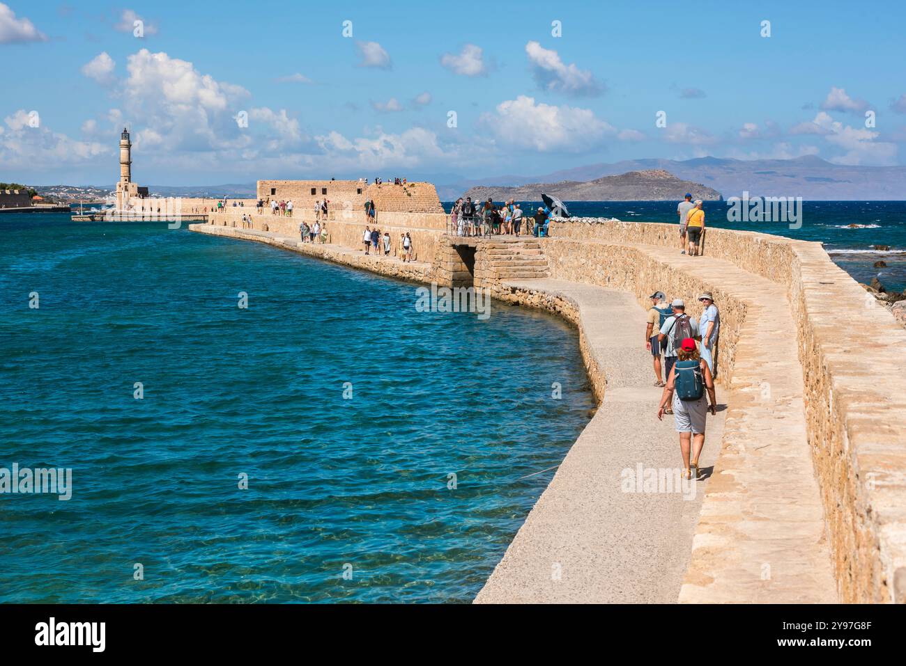 City sea wall Chania, view of tourists walking on the historic sea wall that encloses the Venetian old town harbour area in Chania, Crete, Greece Stock Photo
