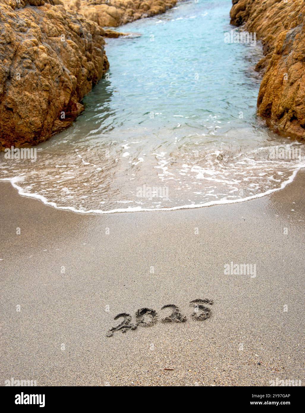 Wave Passing Between Two Rocks 2025 handwritten on the sand of a beach with a wave passing between ...