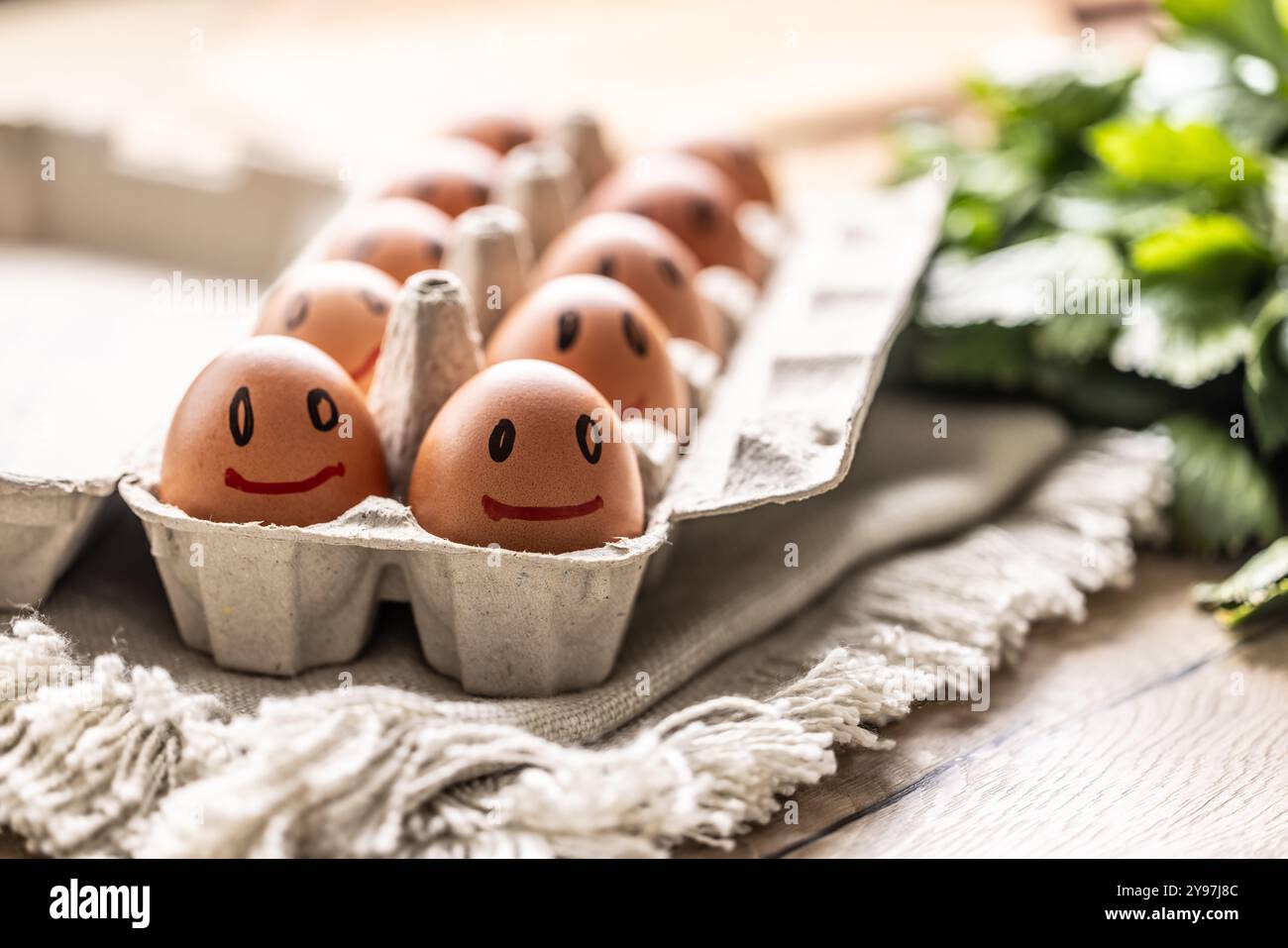 Cute smiling fresh eggs in a paper carton on the kitchen table. Stock Photo