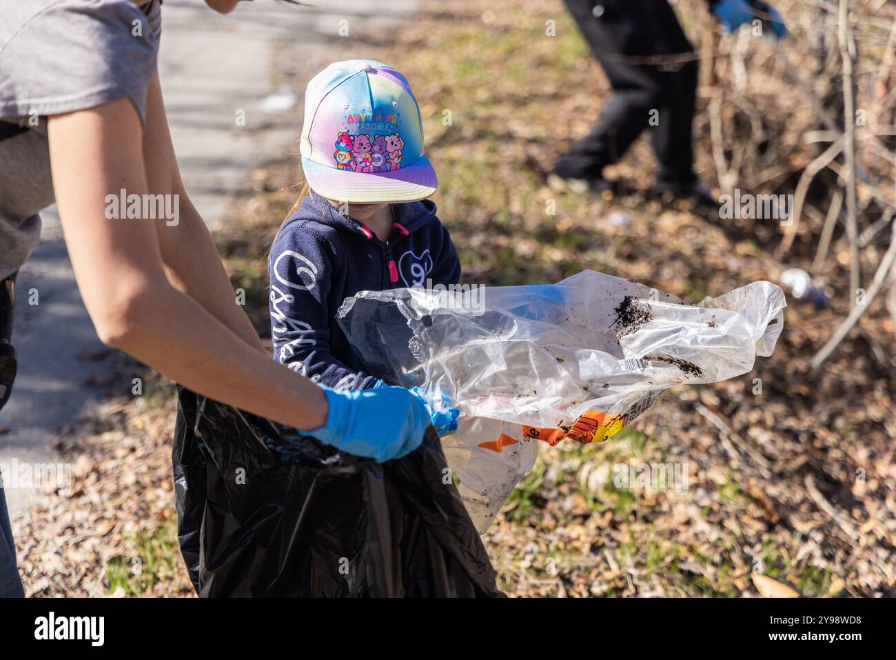 Young volunteer is putting trash in a garbage bag while her mother ...