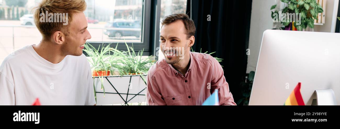 Two smiling men share a light hearted conversation while working together in a bright room. Stock Photo