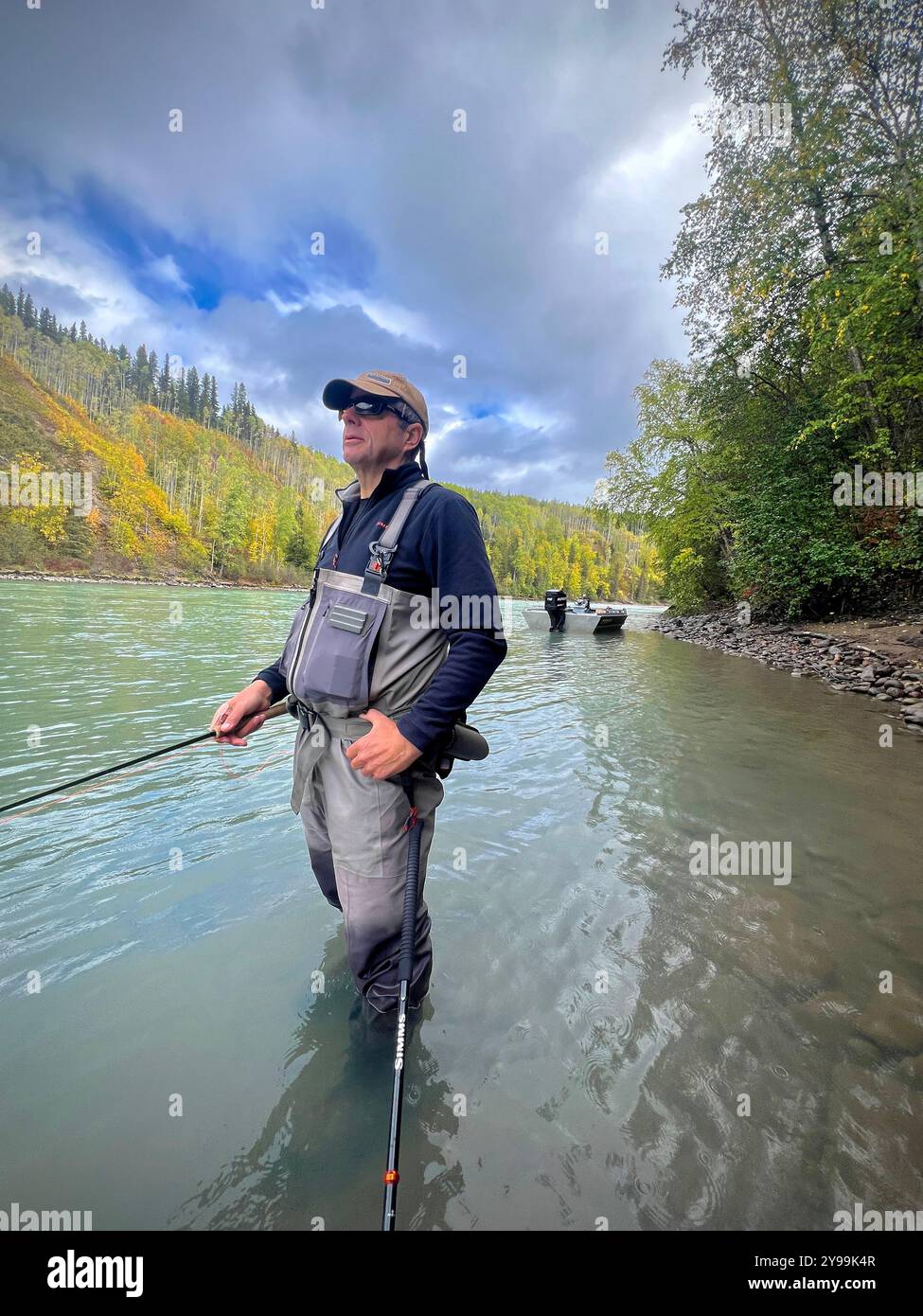 Angler steelhead fishing in the scenic Bulkley Valley, British Columbia, standing in a river surrounded by fall foliage and mountainous terrain - Smartphone Captured Stock Image