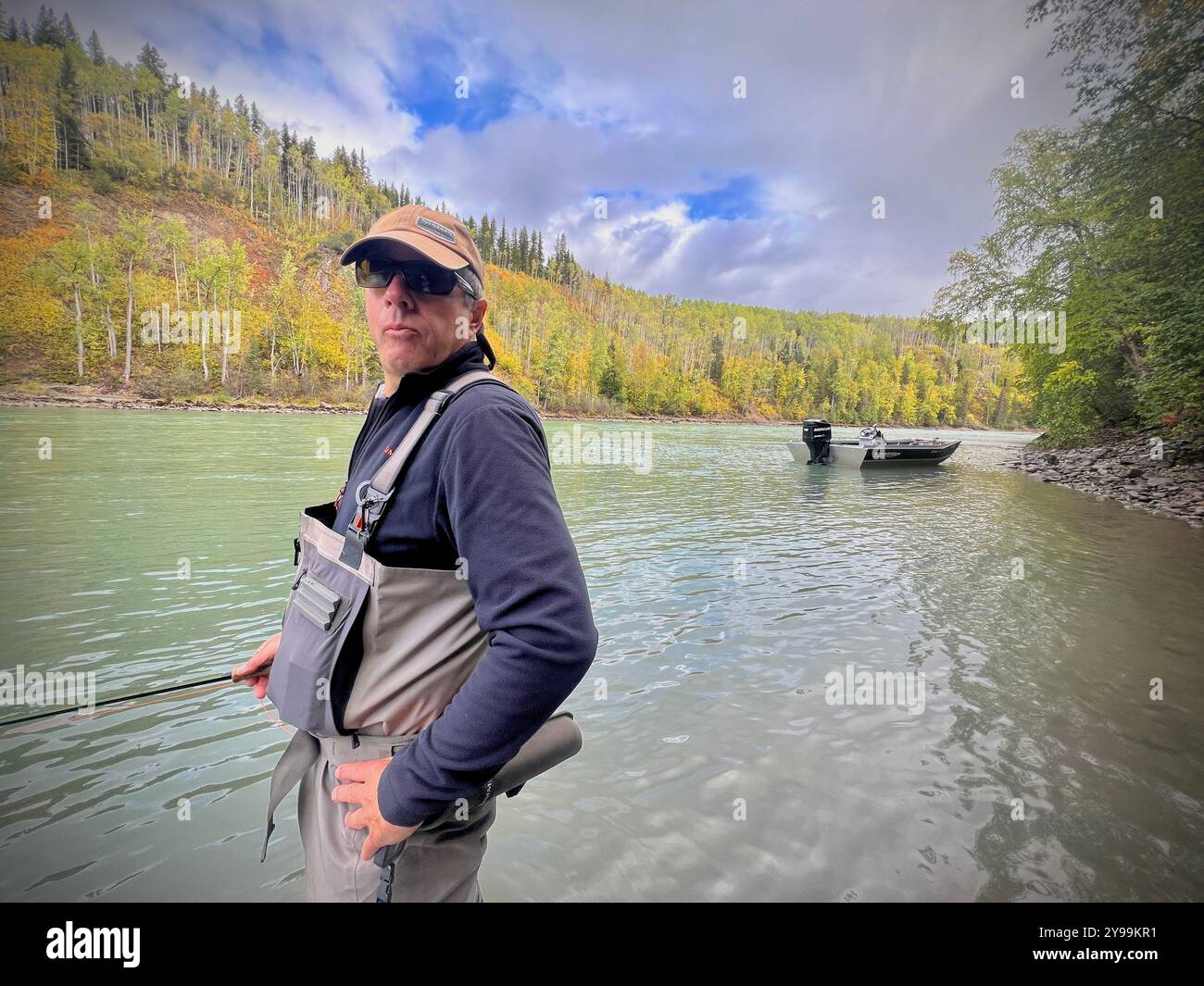 Angler steelhead fishing in the scenic Bulkley Valley, British Columbia, standing in a river surrounded by fall foliage and mountainous terrain - Smartphone Captured Stock Image