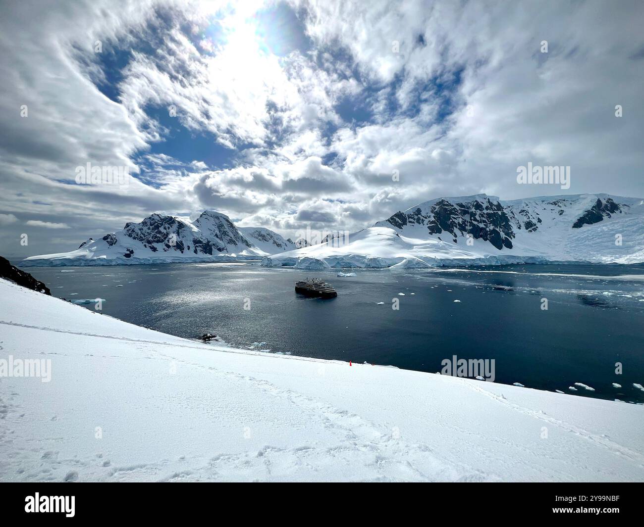 National Geographic Endurance anchored in a pristine bay at Graham Land, Antarctica, surrounded by dramatic snowy peaks and icy waters - Smartphone Captured Stock Image