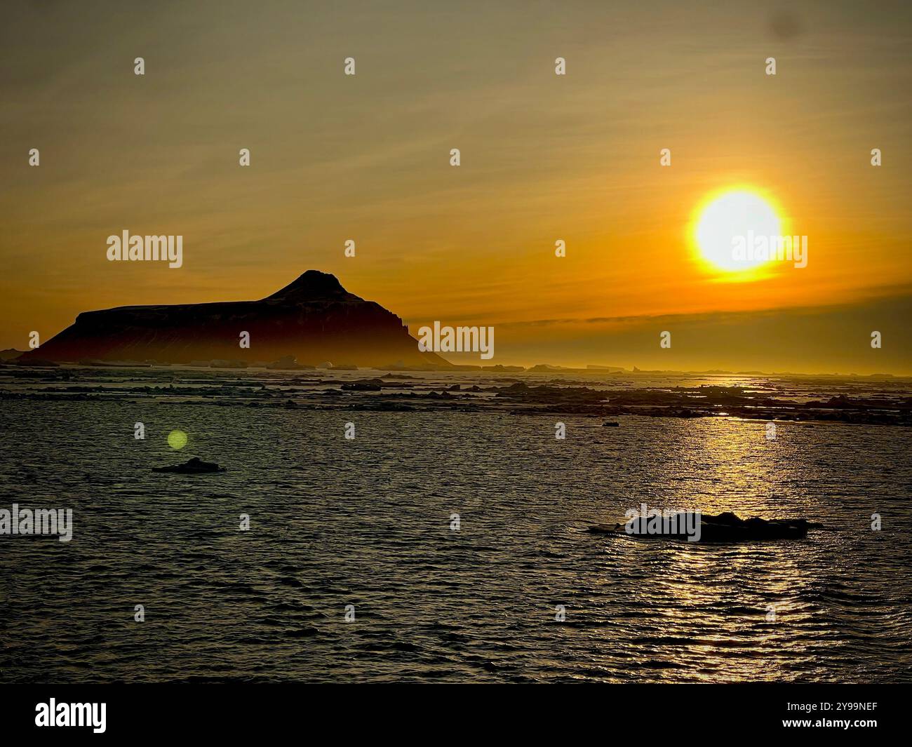A golden sunset over the icy waters of the Southern Ocean, casting warm light on the distant mountain. A serene moment in Antarctica’s wilderness - Smartphone Captured Stock Image
