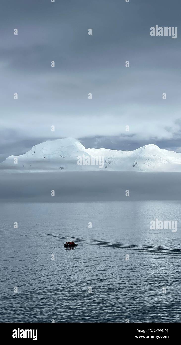 A small expedition boat carrying passengers explores the calm waters of the Southern Ocean with snow-capped mountains in the background in Antarctica - Smartphone Captured Stock Image