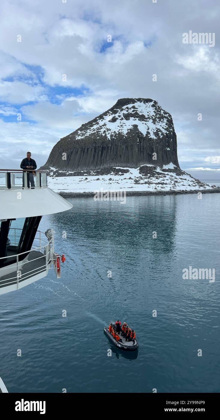 Passengers aboard the Lindblad Nat Geo Endurance observe a small expedition boat as it navigates the calm waters near Edinburgh Rock in Antarctica - Smartphone Captured Stock Image