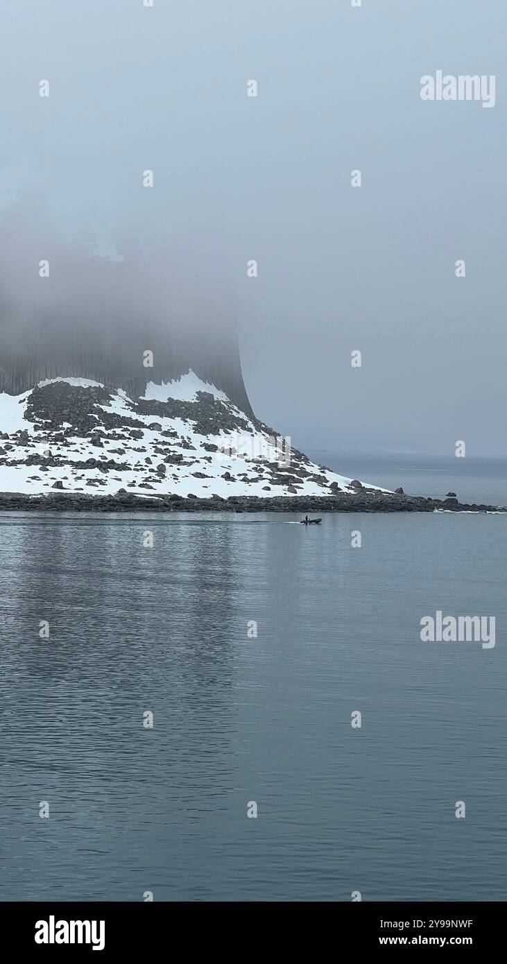 A small expedition boat navigates through the misty waters near the snow-covered Edinburgh Rock in Antarctica - Smartphone Captured Stock Image