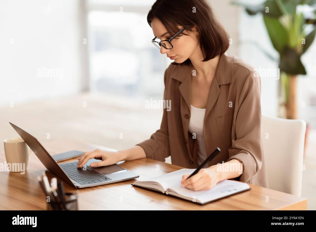 Portrait of manager using pc and writing in notebook Stock Photo - Alamy