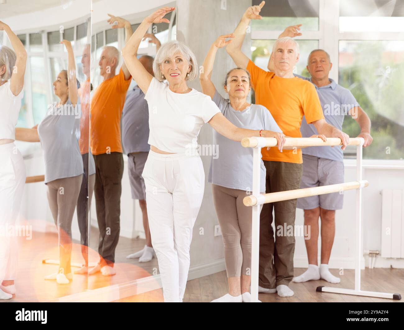 Active mature woman practicing third position holding by ballet barre ...