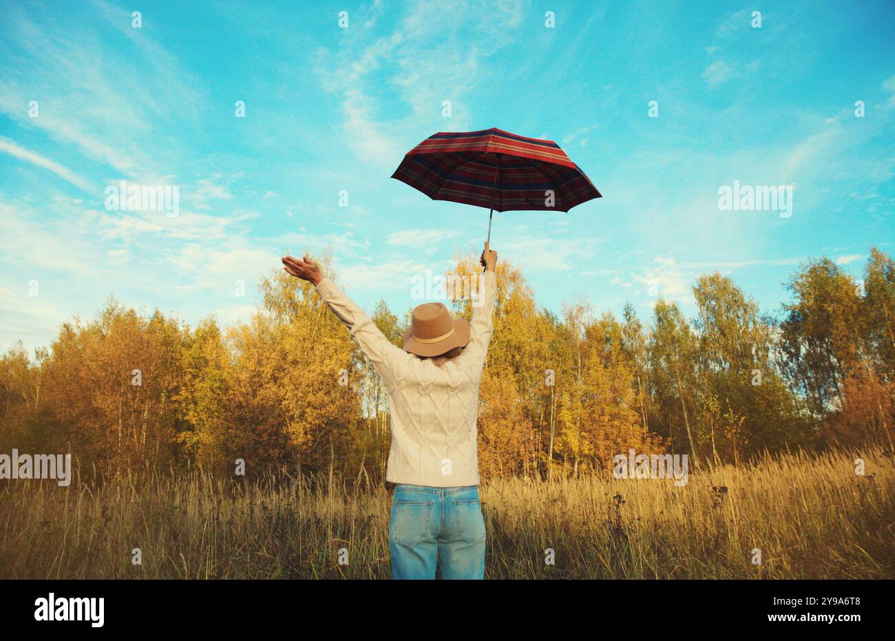 Back view, happy woman in autumn park raising her hands up with umbrella, enjoying warm sunny weather Stock Photo