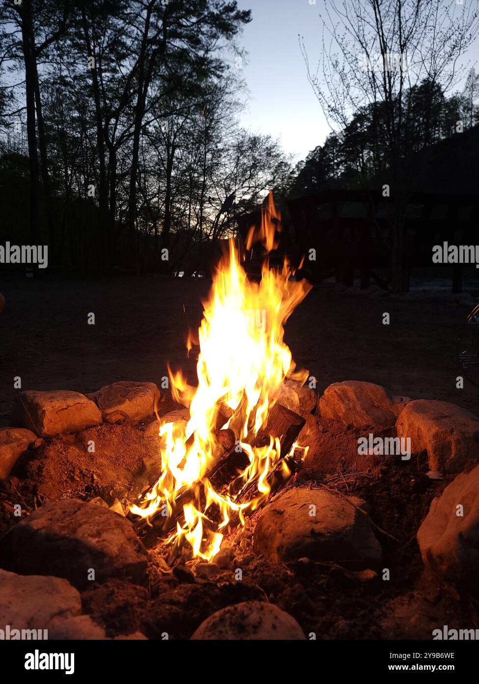 A warm glowing campfire in the Georgia mountainside right by a flowing river at night. - Smartphone Captured Stock Image