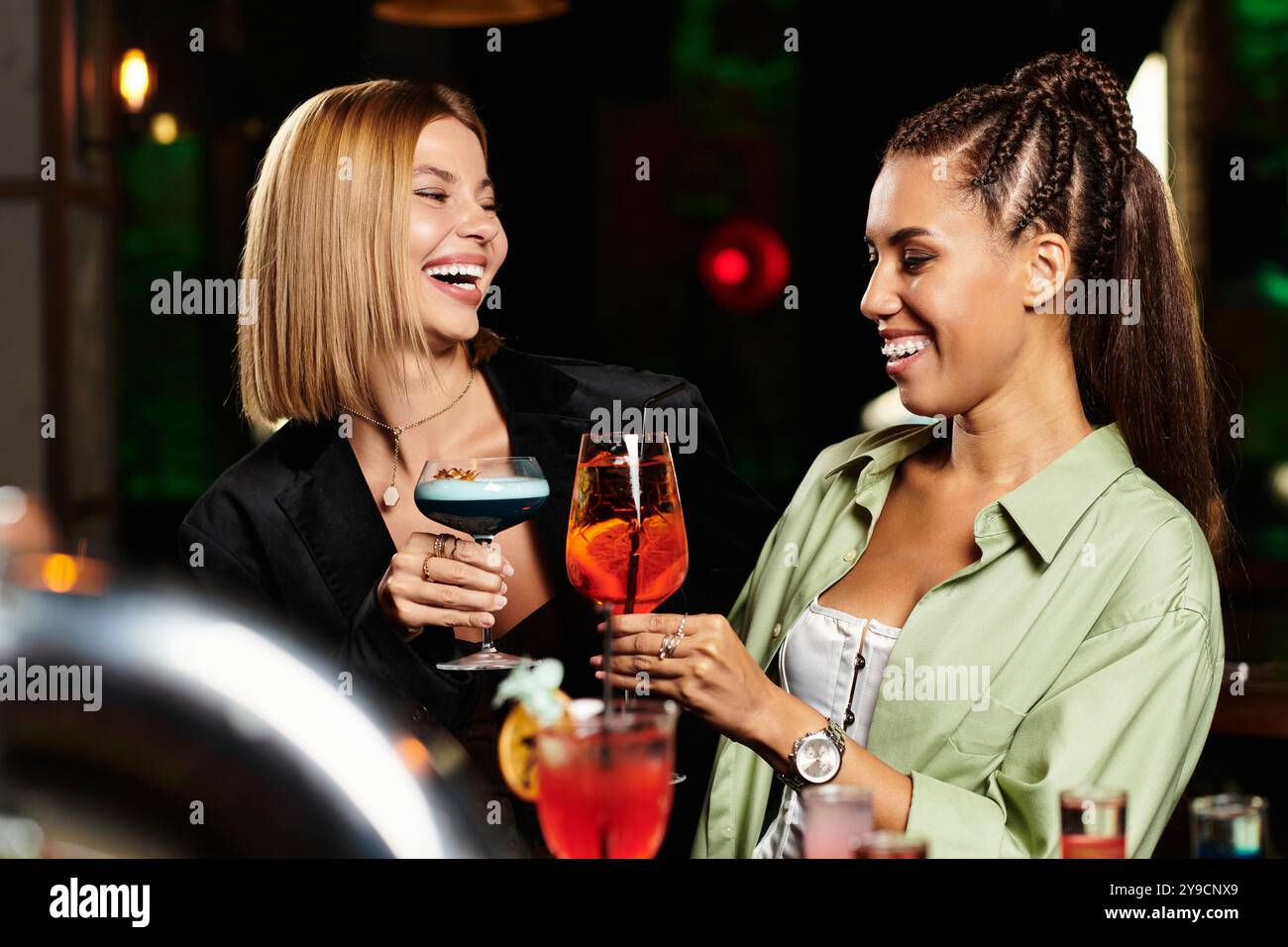 Two young professionals share a moment of joy while toasting with colorful cocktails at a party. Stock Photo