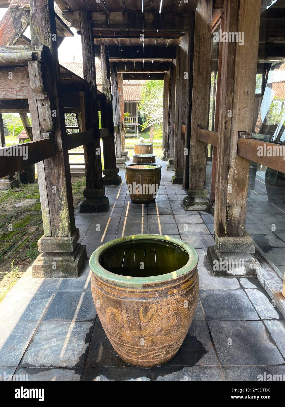 Underneath a traditional wooden house, the strong timber pillars and beautifully crafted joints support a rich history, while a clay jar adds a touch. - Smartphone Captured Stock Image