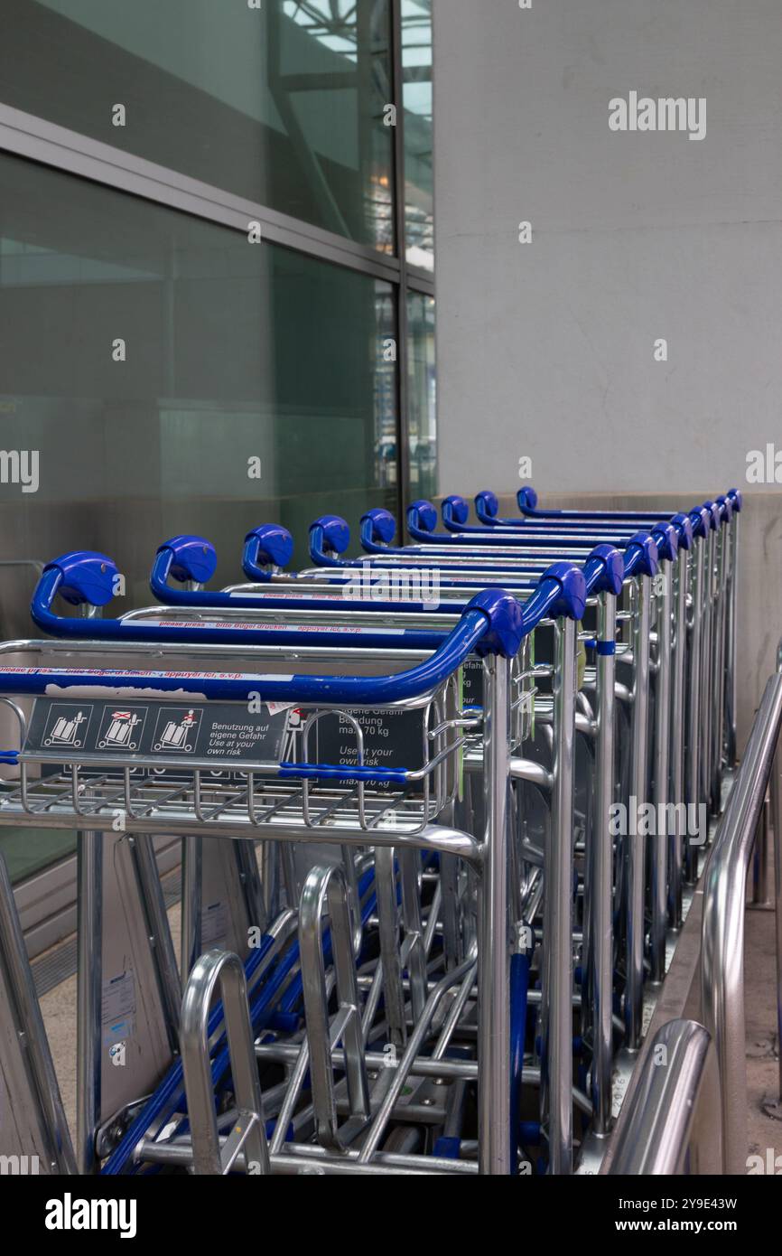 A row of empty luggage carts is neatly aligned in a contemporary airport terminal. Stock Photo