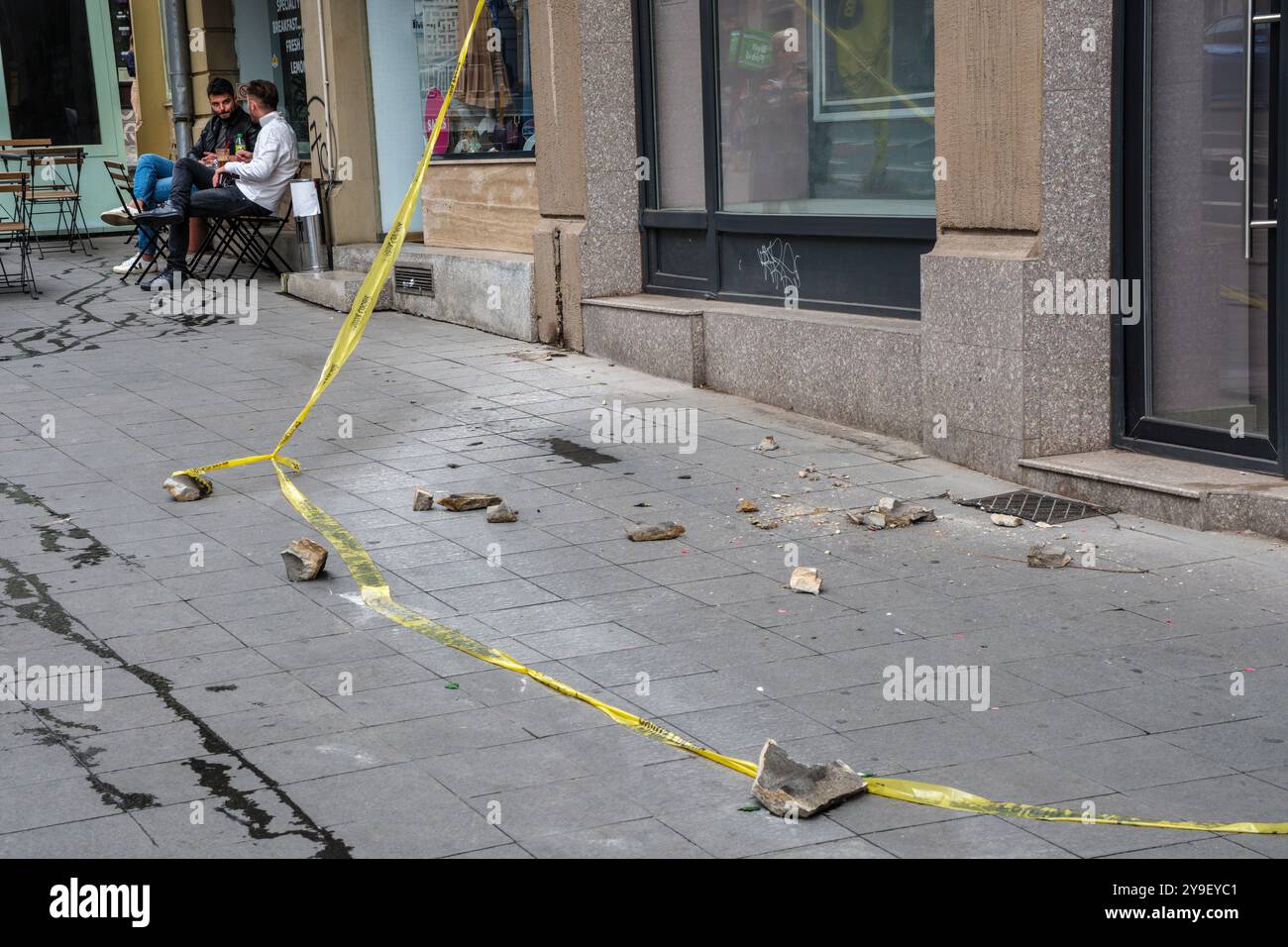 Two men relax at a café table, unfazed by the chunks of masonry that have fallen from the nearby Adriatica Trieste Block, an old building in Bucharest Stock Photo