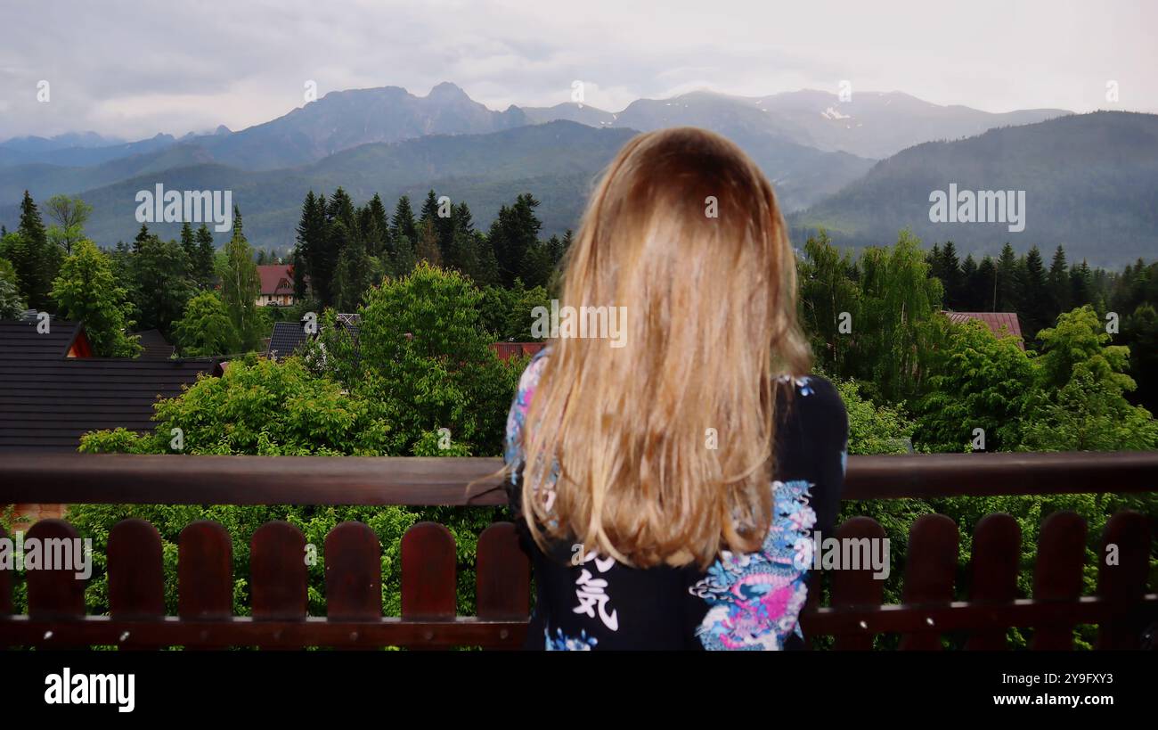 A woman stands with her back facing the camera, gazing at a mountain ...