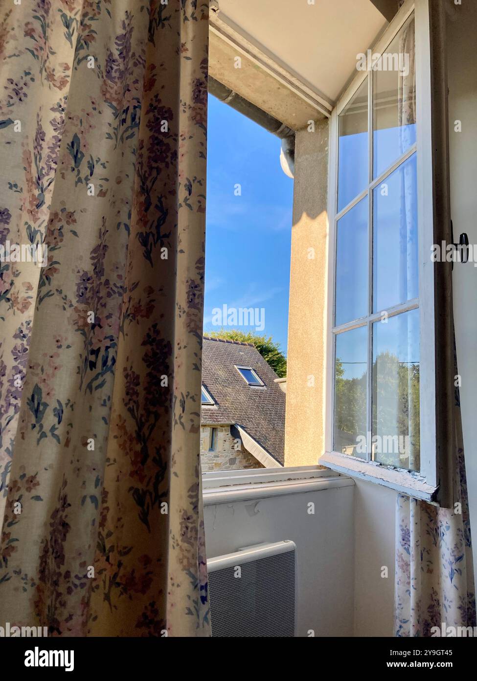 An open lattice window with curtains with flower pattern in a traditional Breton home, blue sky outside, view from the inside - Smartphone Captured Stock Image