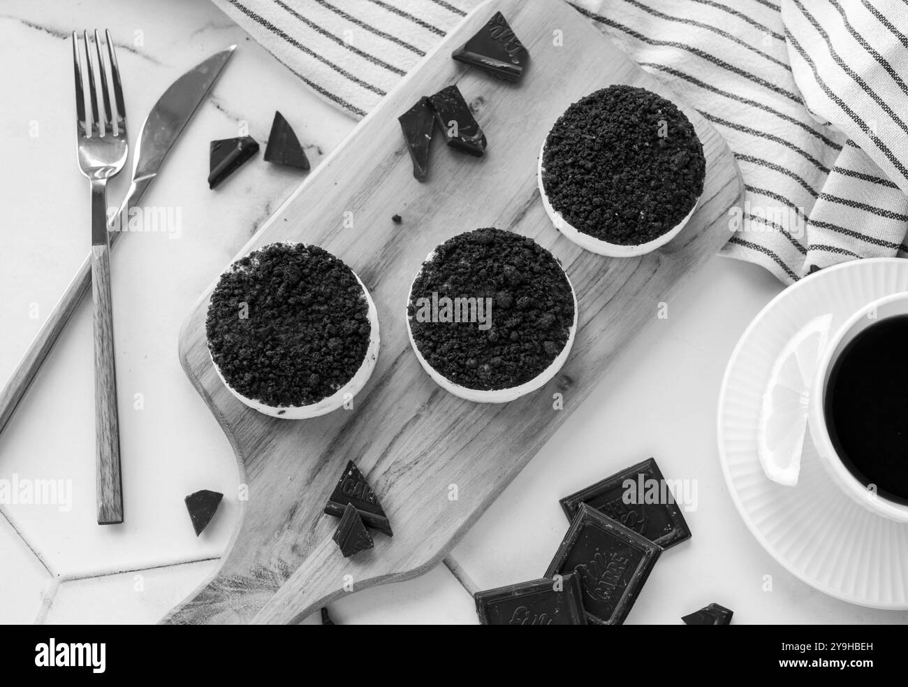 Top view of mini chocolate chip cheesecakes on a wooden board with a cup of black coffee in a monochromatic setting.  Stock Photo