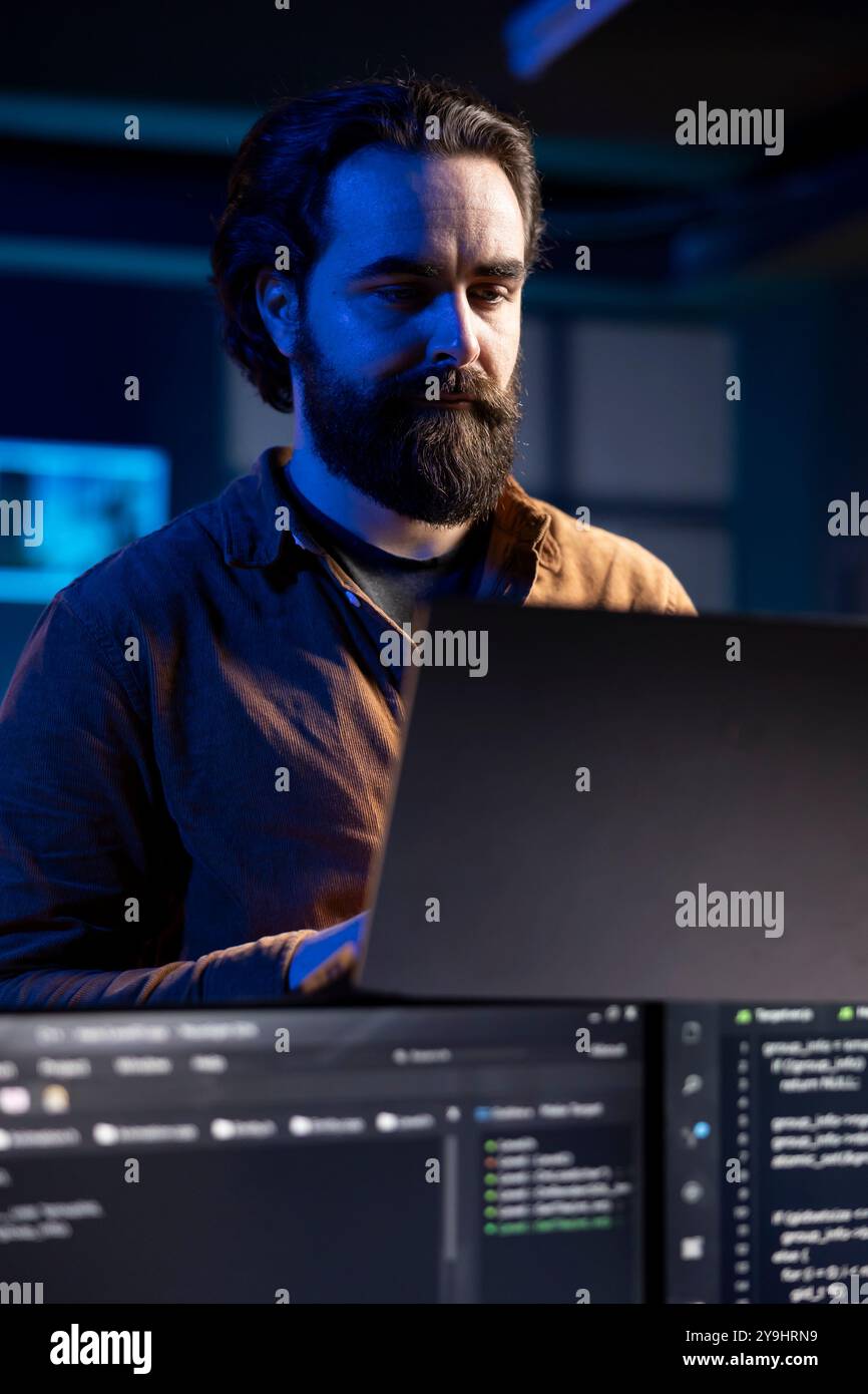 Teleworking IT admin working from RGB lit home using laptop, testing and deploying programs and systems. Software technician checking code displayed on computer screens, standing in apartment Stock Photo