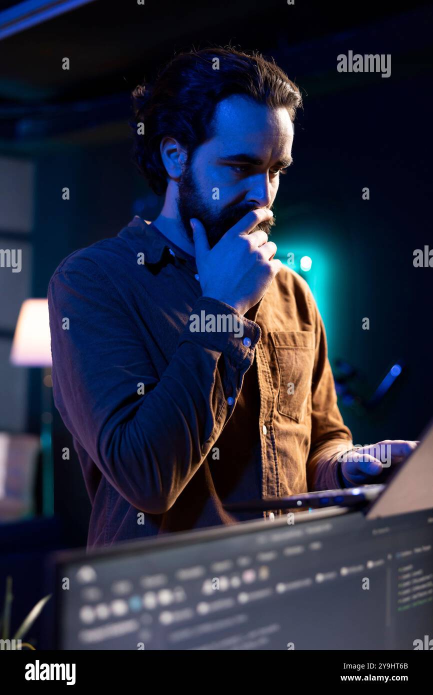 Pensive man developing software in Java programming language using laptop, examining. Contemplative programmer walking through apartment thinking how to solve coding issues Stock Photo