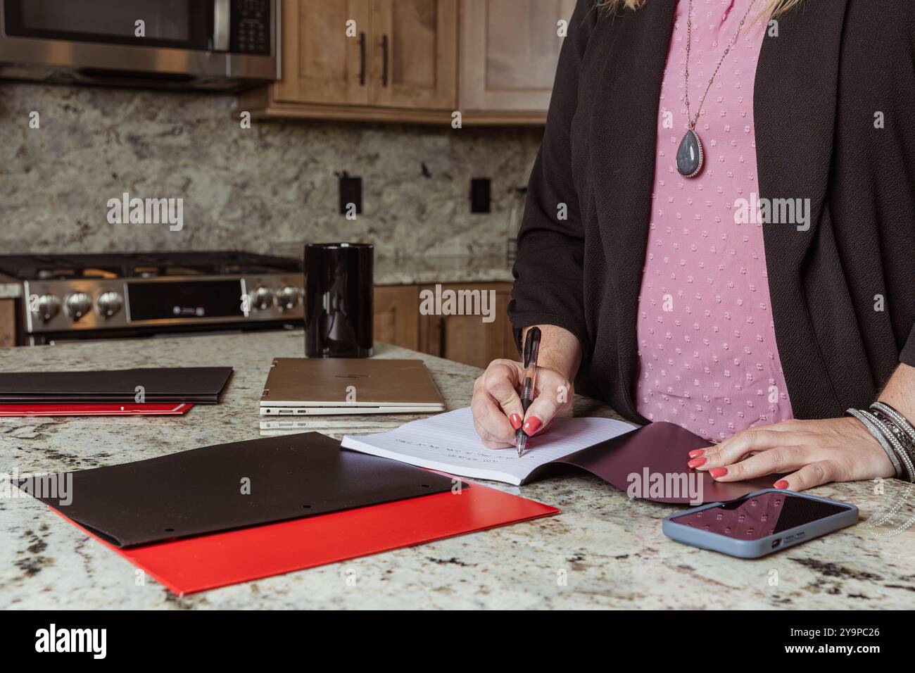 Close-up of a woman writing in a notebook on a kitchen counter Stock Photo