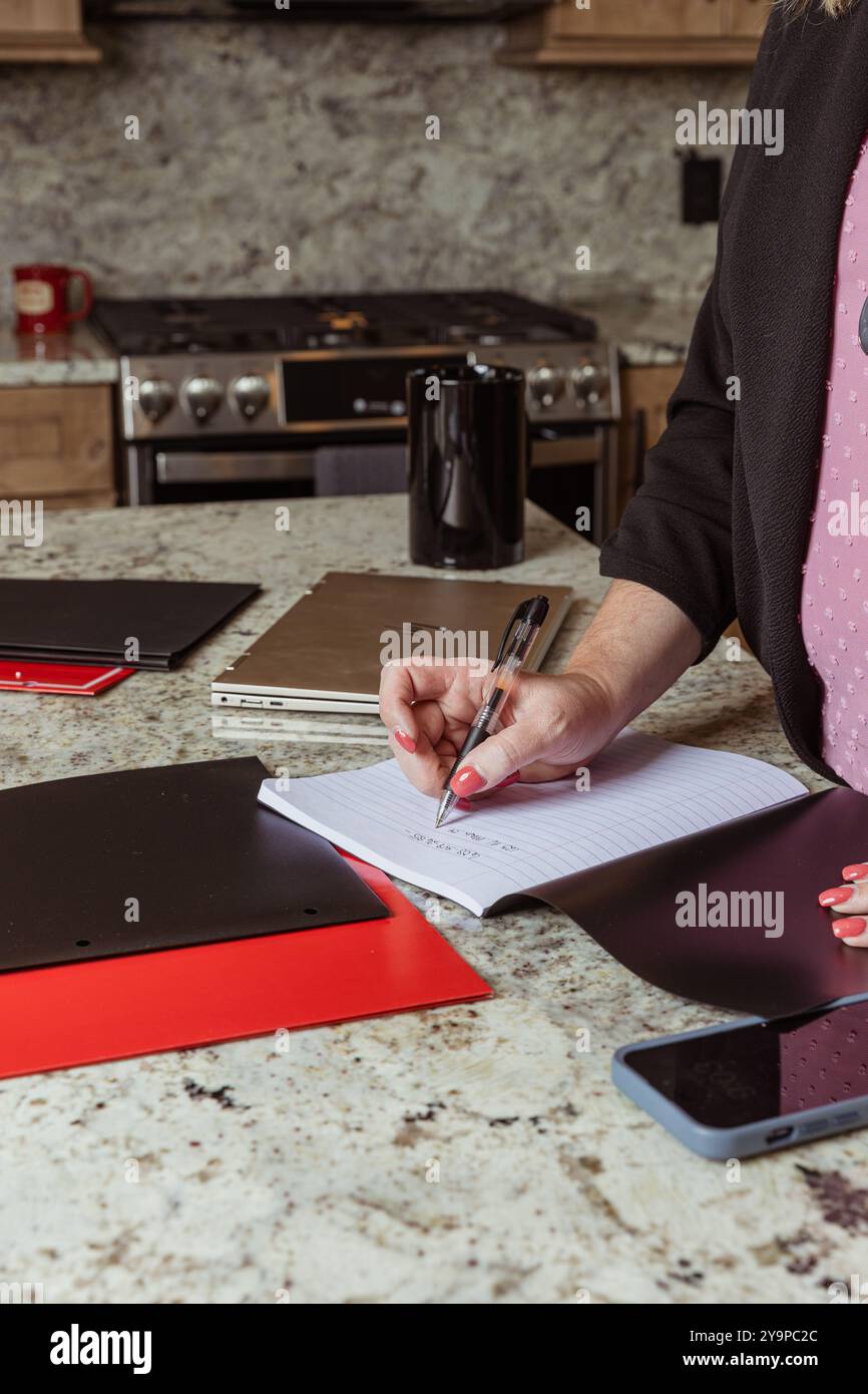 Close-up of a woman writing in a notebook on a kitchen counter Stock Photo
