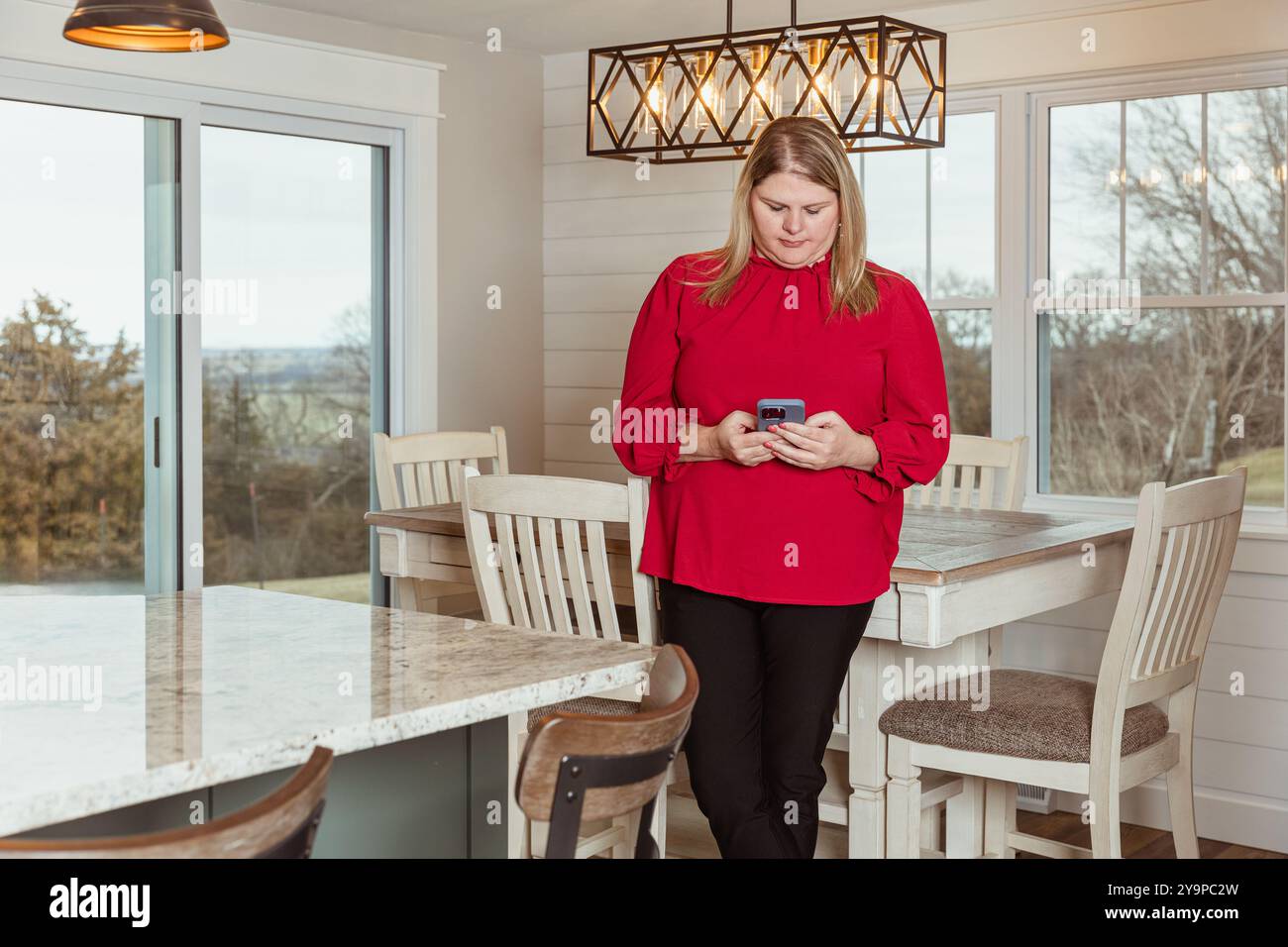 Woman on the phone, standing in a kitchen Stock Photo