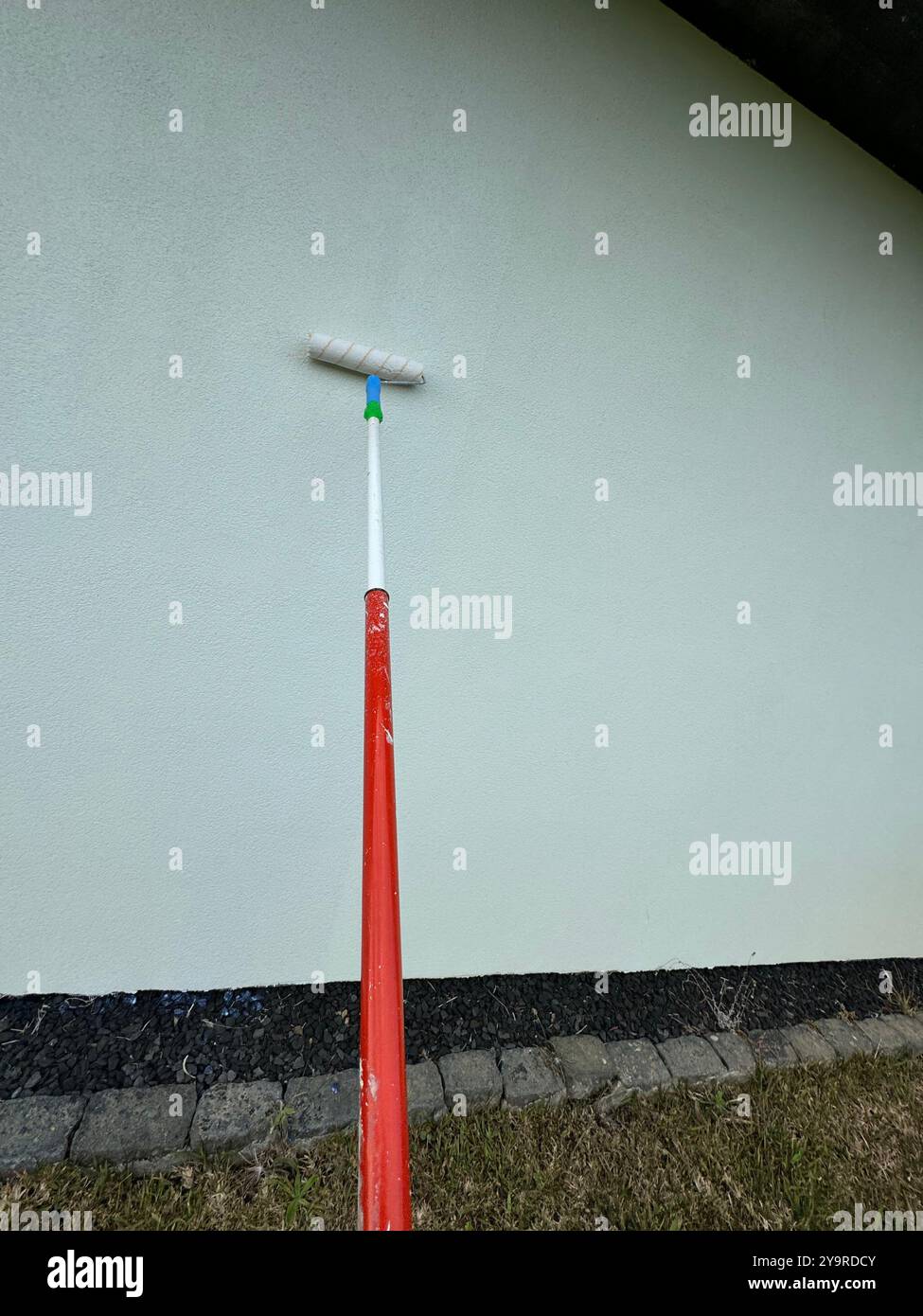 Painting a house exterior with a roller on an extension pole for a fresh white finish. - Smartphone Captured Stock Image
