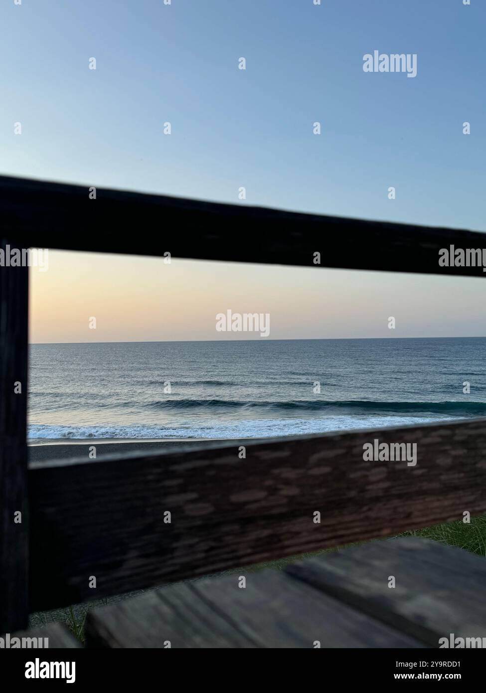 Sunset over the Atlantic Ocean viewed through a wooden railing on the Ribeira Grande seafront, São Miguel Island, Azores. - Smartphone Captured Stock Image
