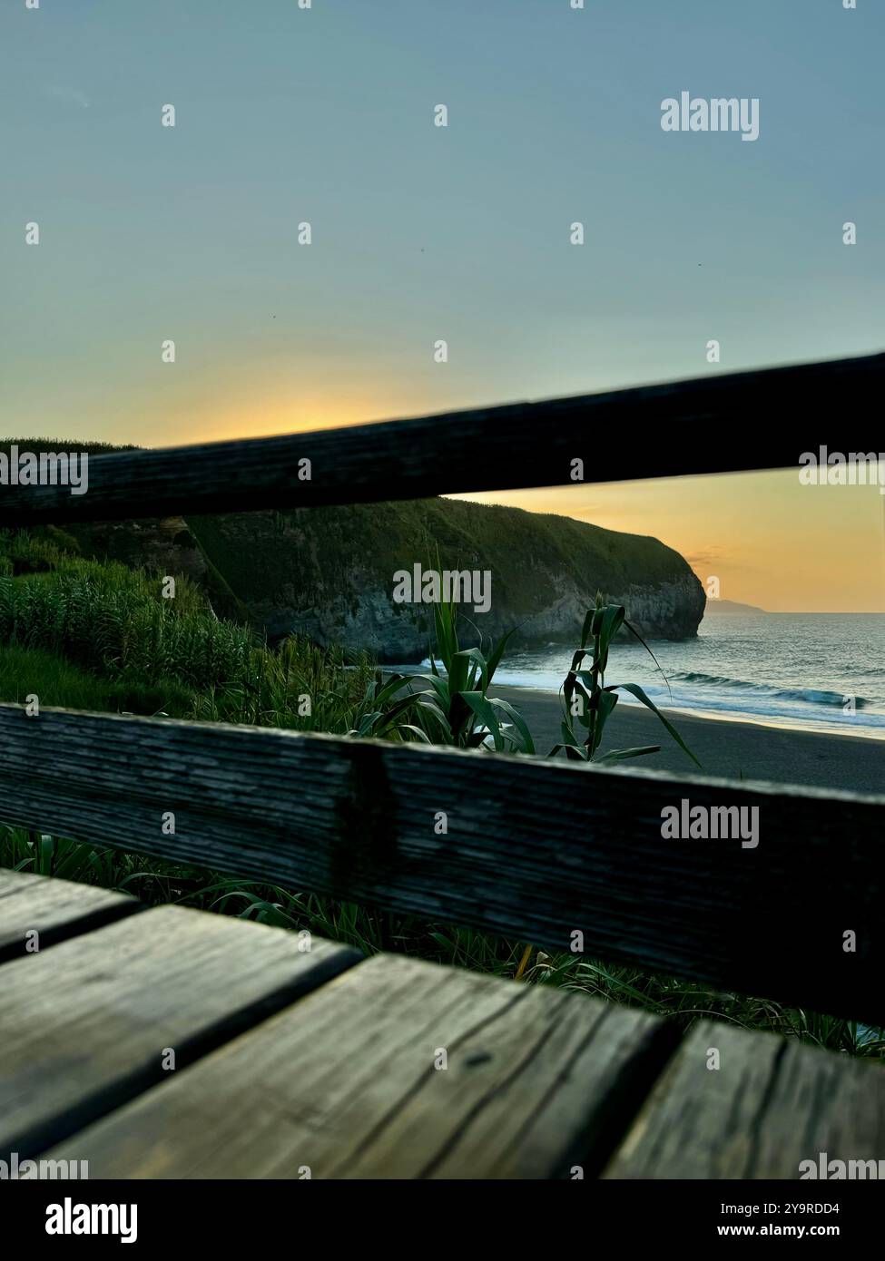 Sunset view over Ribeira Grande Bay framed by wooden railing on São Miguel Island, Azores. - Smartphone Captured Stock Image