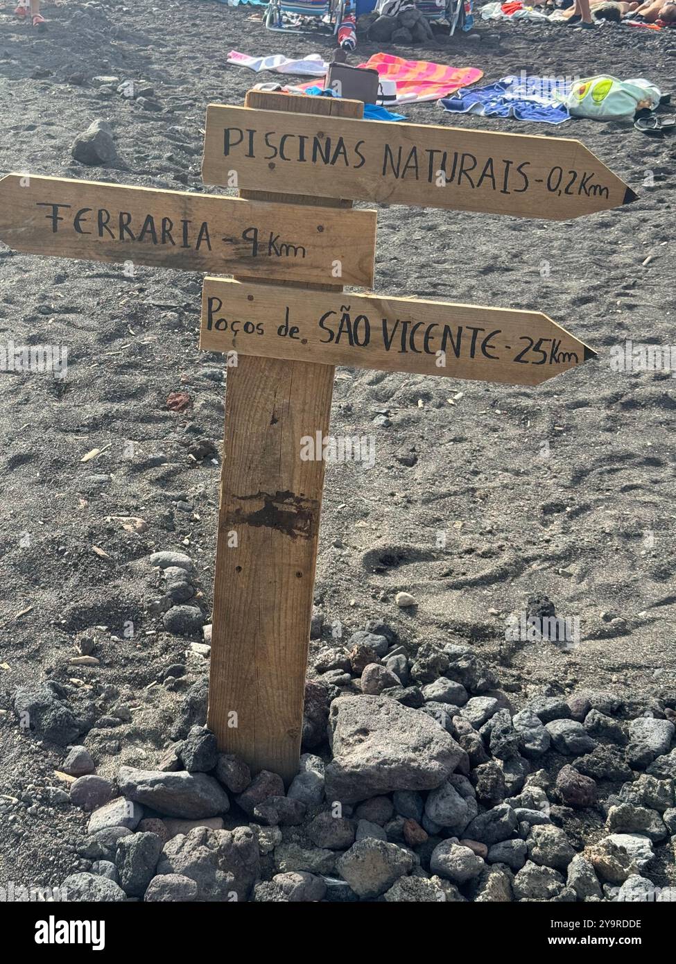 Wooden directional signpost to “Piscinas Naturais” and local landmarks on a black‑sand beach in Mosteiros, São Miguel Island, Azores. - Smartphone Captured Stock Image