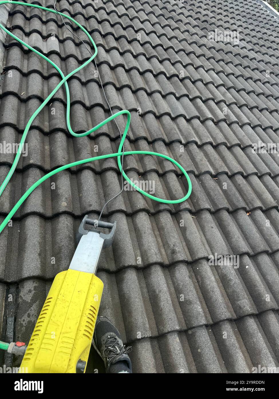 Pressure‑washing roof tiles with a high‑pressure cleaner to remove moss and dirt buildup. - Smartphone Captured Stock Image