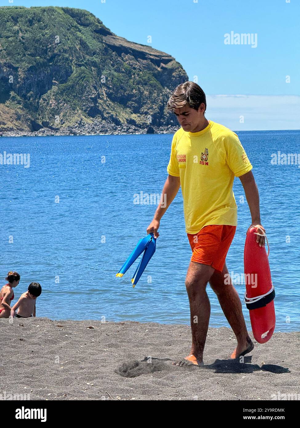 Lifeguard on a black sand beach in São Miguel Island, Azores, Portugal, with flippers and rescue can, on a sunny summer day. - Smartphone Captured Stock Image