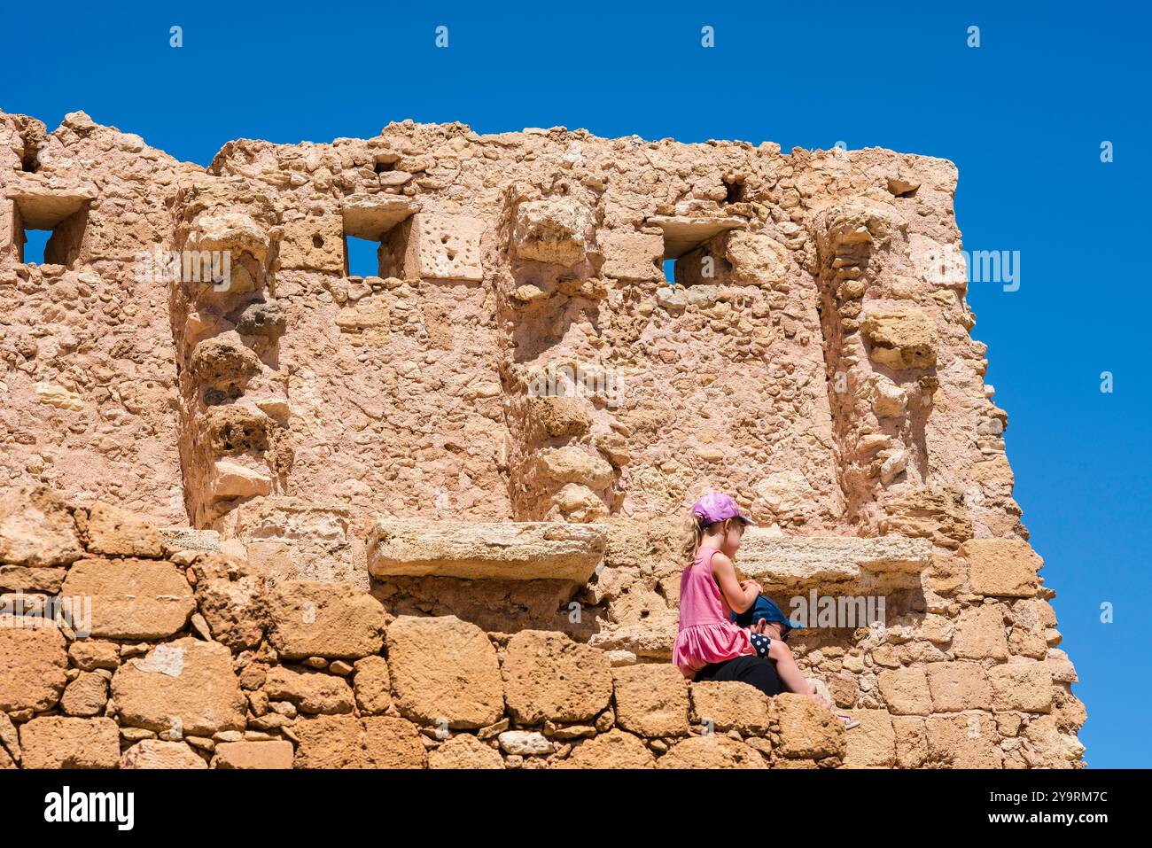 Father daughter travel, view in summer of a young female child being carried on her father's shoulders as they explore ancient ruins in Crete, Greece Stock Photo