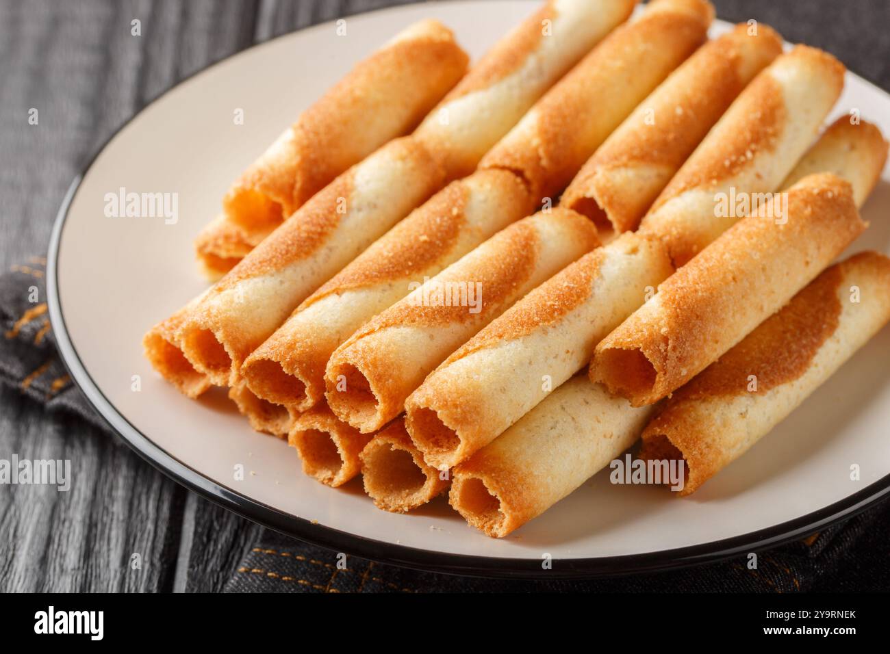 Cigarettes russes or russian cigarettes is a baked thin waffle rolls  closeup on the plate on the table. Horizontal Stock Photo