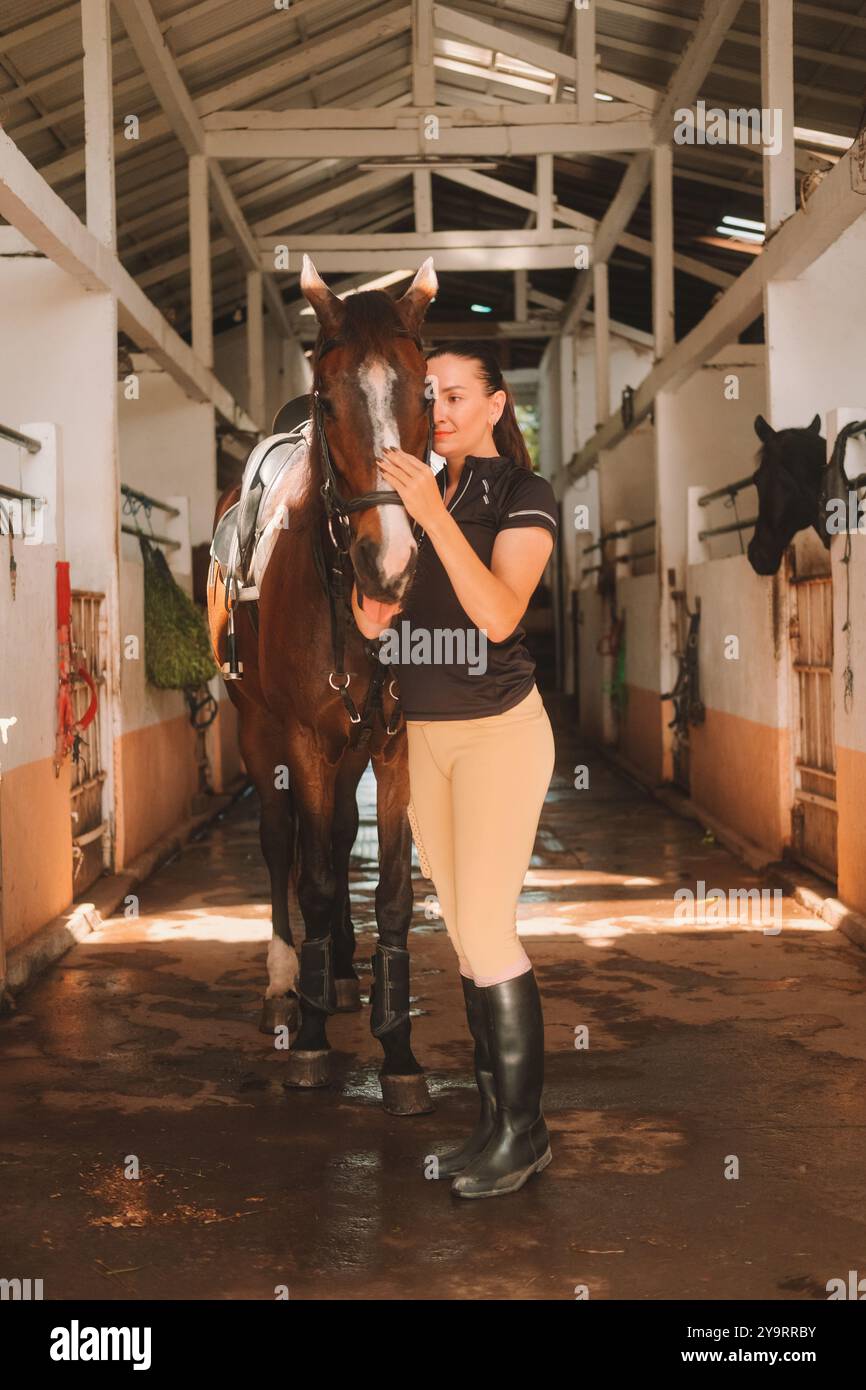 Young woman rider in equestrian uniform standing in stable next to her ...