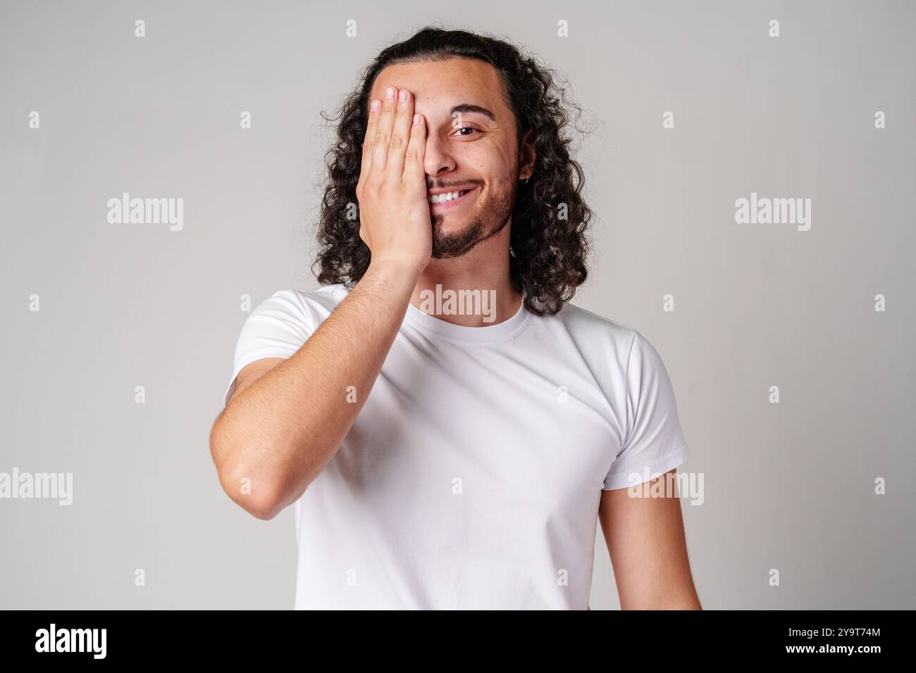 A young man playfully covering one eye with his hand while smiling in a ...