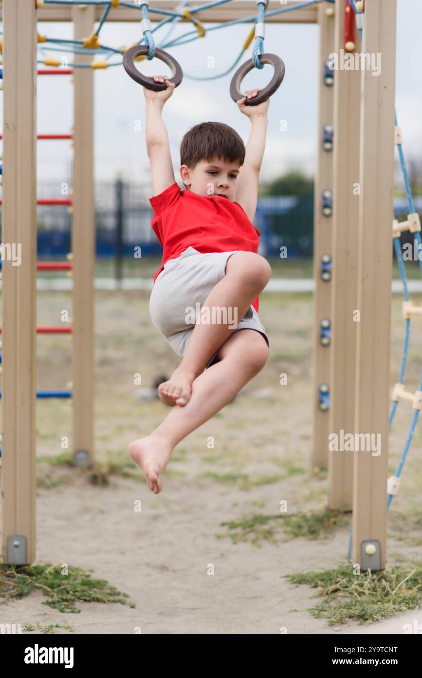 Happy boy playing and hanging on rings on playground. Kids exercises ...