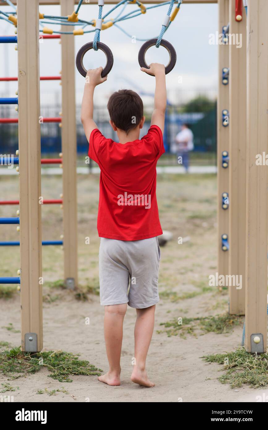 Happy boy playing and hanging on rings on playground. Kids exercises ...