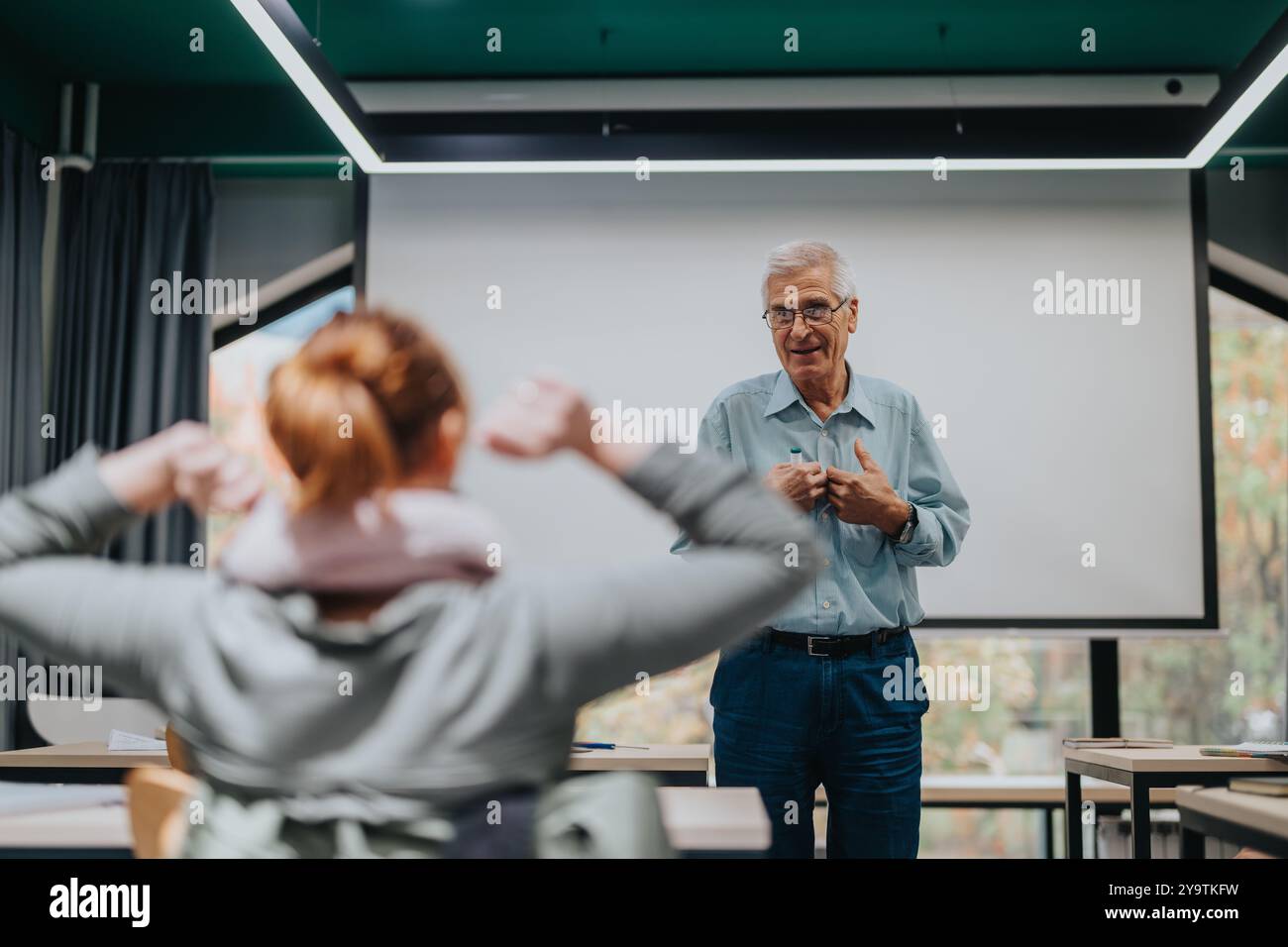 Elderly professor engaging with students in a modern classroom Stock Photo