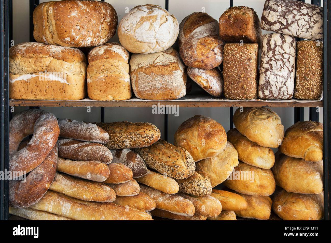 Assorted artisan bread loaves stacked on bakery shelves, sourdough, seeded and rustic breads, fresh baked daily display. Stock Photo