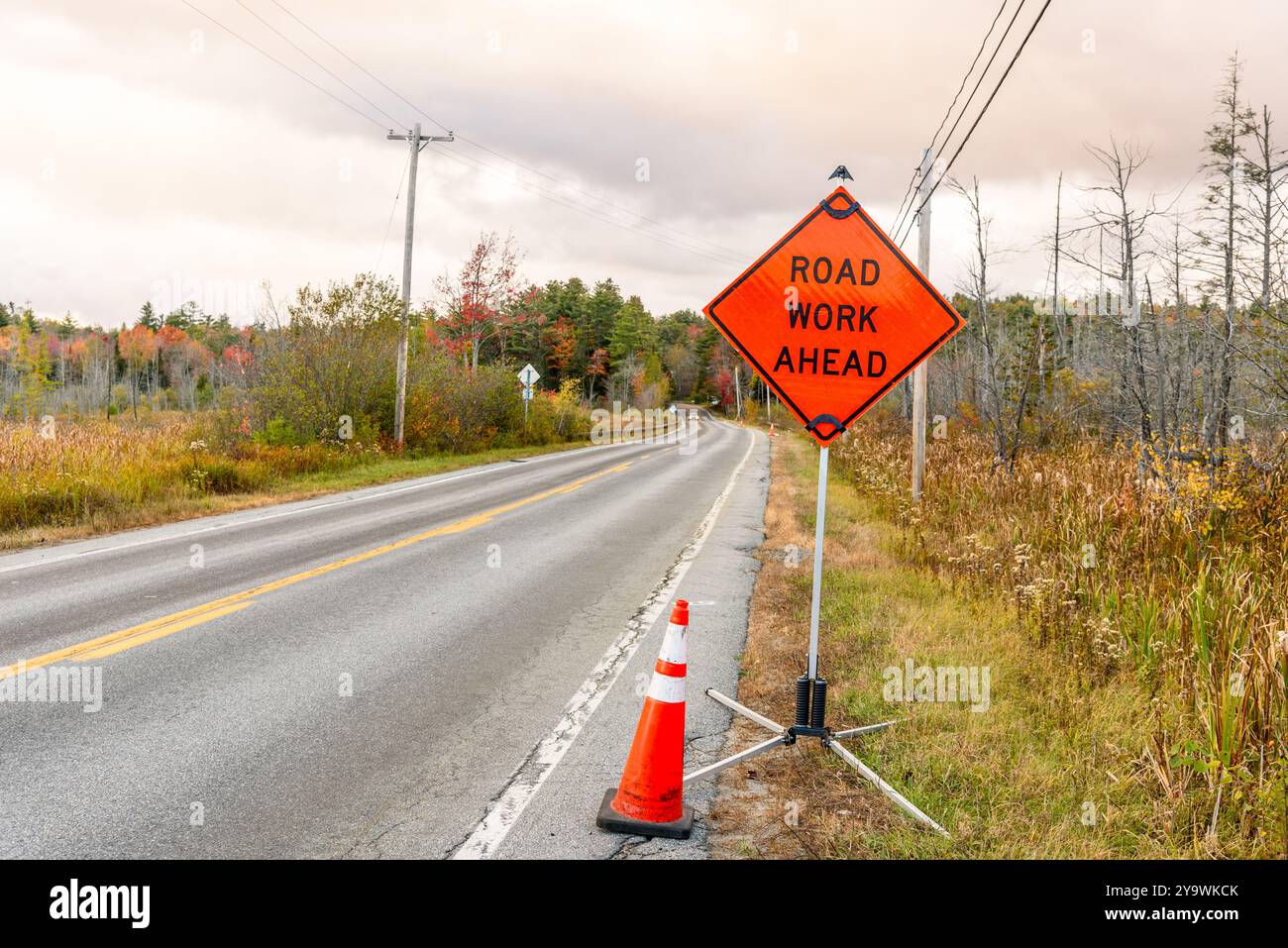 Red warning sign with a traffic cone at the beginning of roadwoks area along a country road on a cloudy day Stock Photo