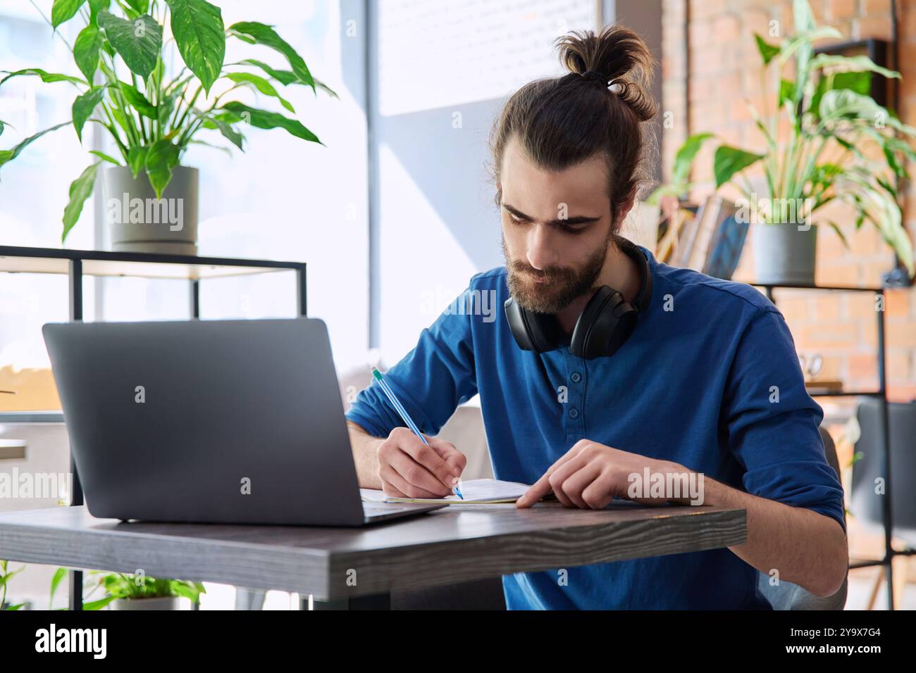 Young male university student studying using laptop, writing in notebook Stock Photo