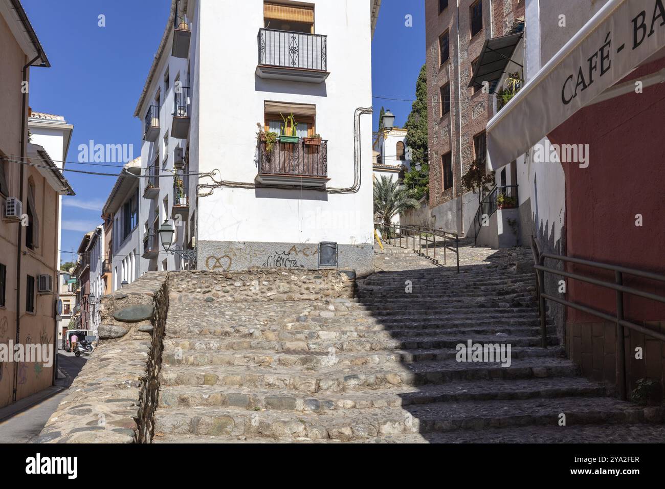 Cobbled cobblestone street with steps and traditional buildings under a blue sky, Granada Stock Photo